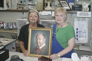 FAMILY BUSINESS: From left, pharmacy technician Barbara Cuevas and Dianne Cruse pose with a painting of Cruse’s late husband Fred Cruse III. Photo by Jeremy Pittari